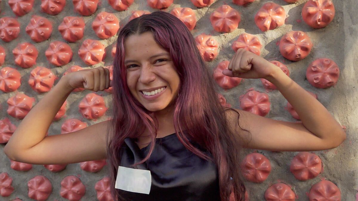 Oriana poses in front of 'chica street', a house she helped to make out of plastic bottles filled with sand.