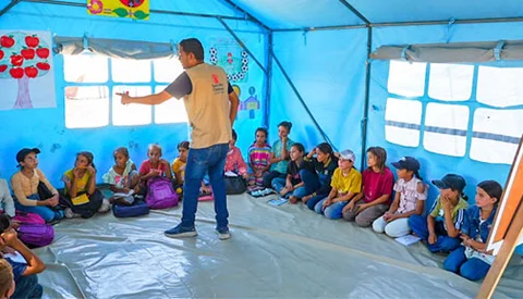 Save the Children docent geeft kinderen les in een noodtent