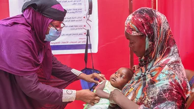 Een medewerker van Save the Children controleert of peuter Safana ondervoed is. Het meisje zit op schoot bij haar moeder.