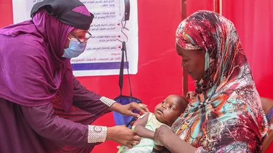 Een medewerker van Save the Children controleert of peuter Safana ondervoed is. Het meisje zit op schoot bij haar moeder.