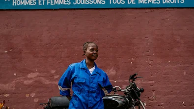 De zestienjarige Bea staat tegen een muur aan met een motor. Boven haar staat de tekst "Mannen en vrouwen hebben dezelfde rechten." in het Frans