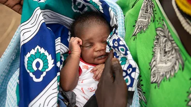 Een baby slaapt in de armen van zijn moeder. Hij is gewikkeld in kleurrijke doeken