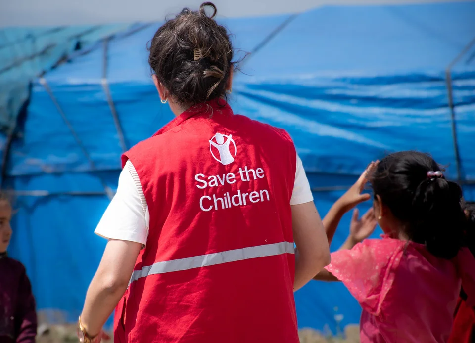 Save the Children Medewerker gezien op de rug voor een blauwe noodtent.