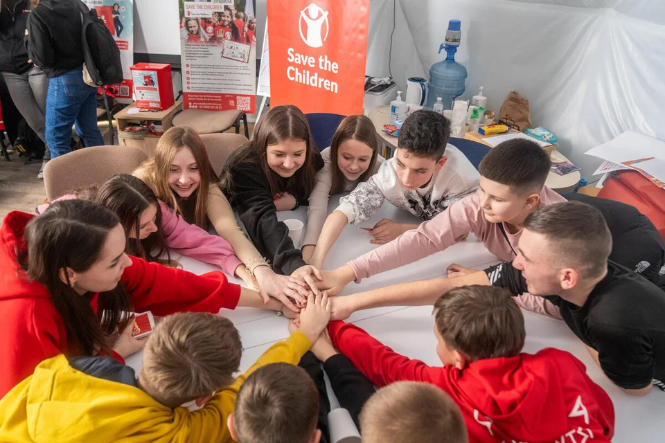 12 kinderen om een ronde tafel leggen een hand op elkaar