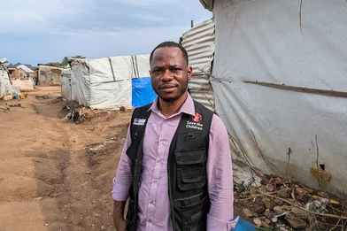 Gabriel staat in een vluchtelingenkamp in de DRC. Hij draagt een zwart Save the Children hesje.