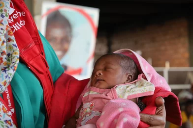 Medewerker van Save the Children houdt een pasgeboren baby vast bij een noodhulpkliniek